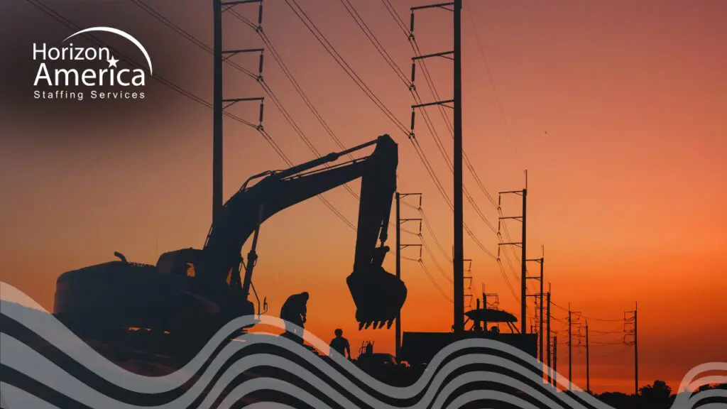 Construction excavator and light industrial worker silhouetted against an orange sunset sky, with power line towers in the background