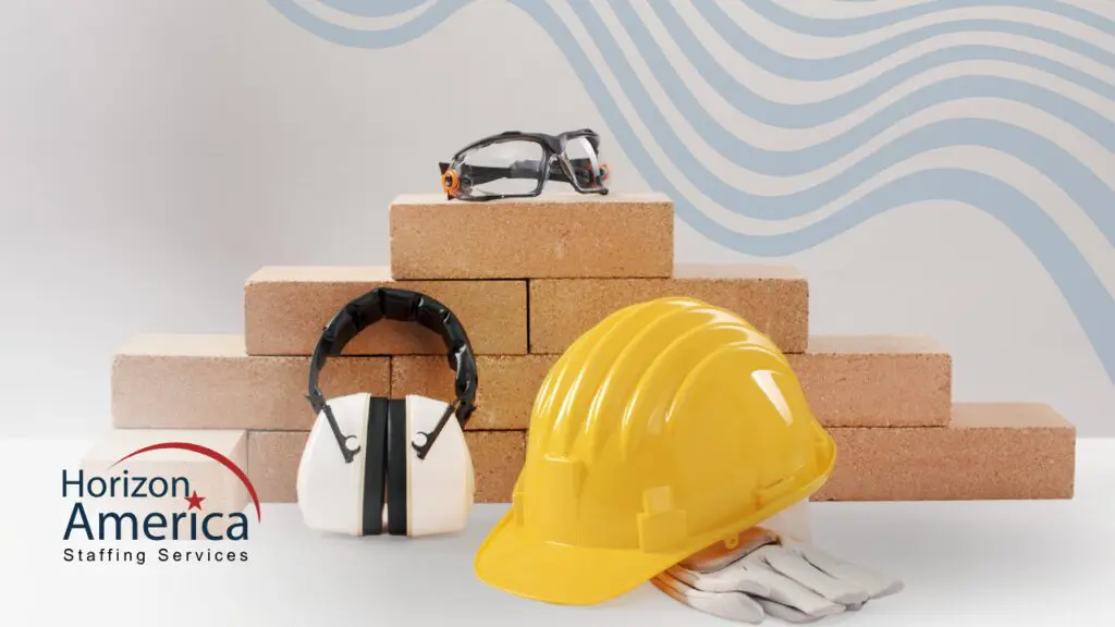 Protective gear—goggles, headphones, hard hat, and gloves—arranged by a stack of bricks