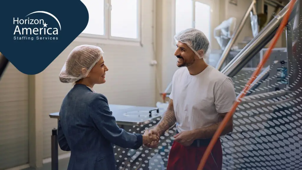 A staffing recruiter and a food processing worker wearing hairnets shake hands on the production floor of a food manufacturing facility.