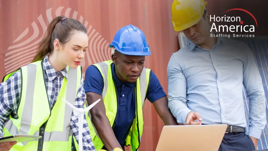 Three distribution operations professionals reviewing staffing metrics on a laptop outside a logistics facility.