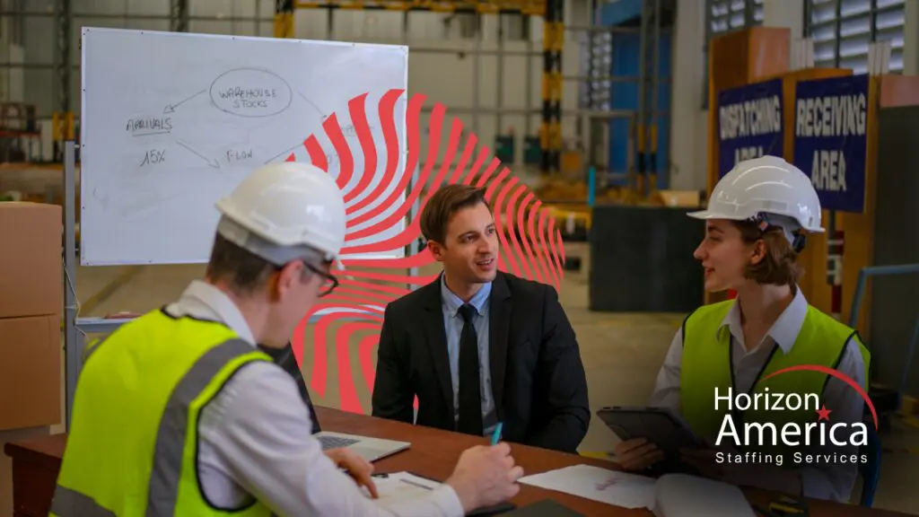 Recruiter meeting with two distribution warehouse employees during a distribution staffing vendor review at a desk near receiving and dispatching areas.