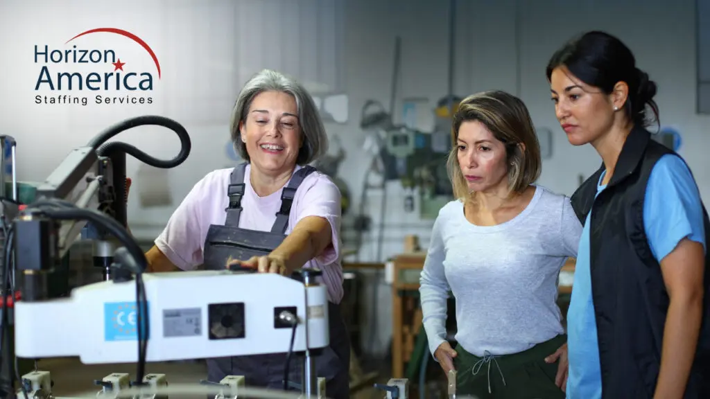 An experienced worker demonstrates an industrial machine to two attentive coworkers in a workshop. Horizon America logo.