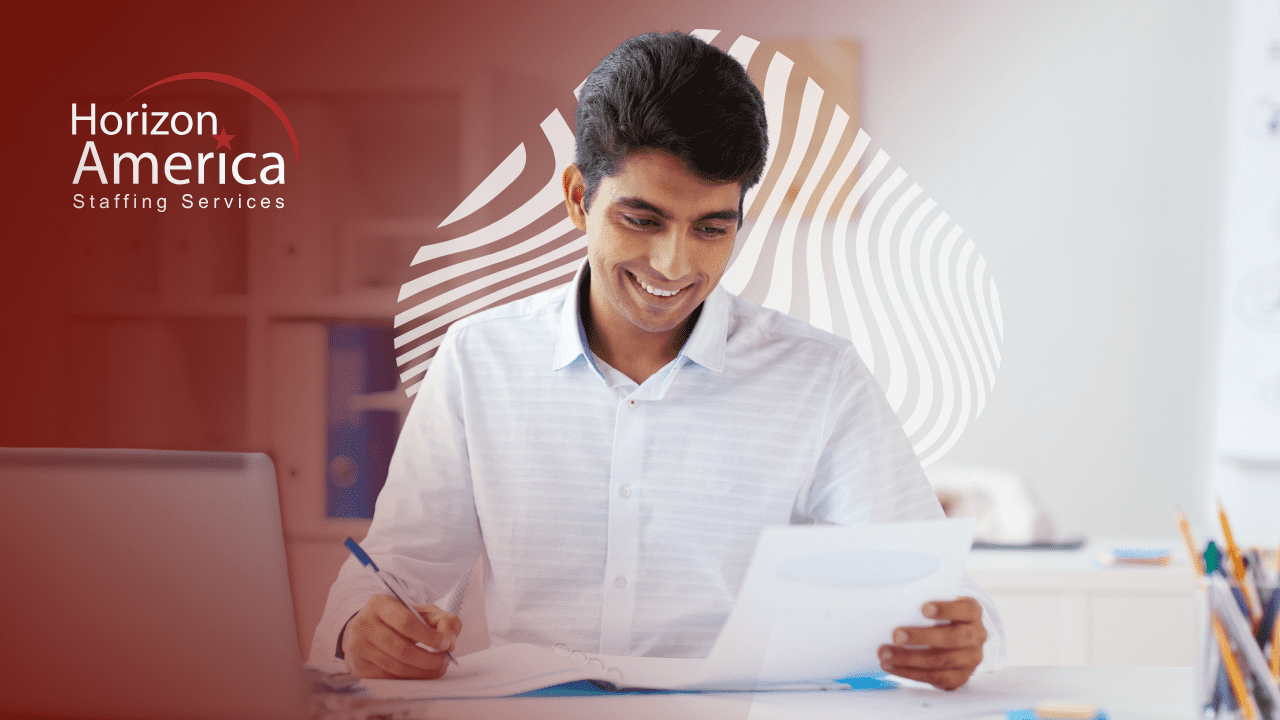 Smiling man in collared shirt taking notes in a binder while looking at a resume