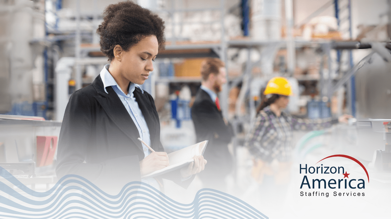 HR staff in corporate attire stands writing in a notebook in an industrial plant