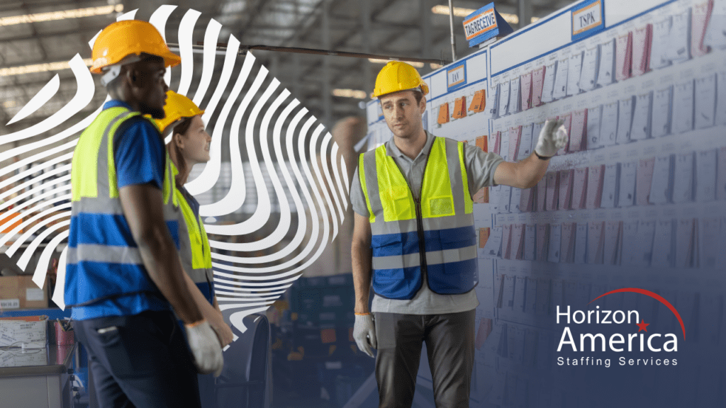 Three warehouse associates in hard hats and safety vests discuss schedules.